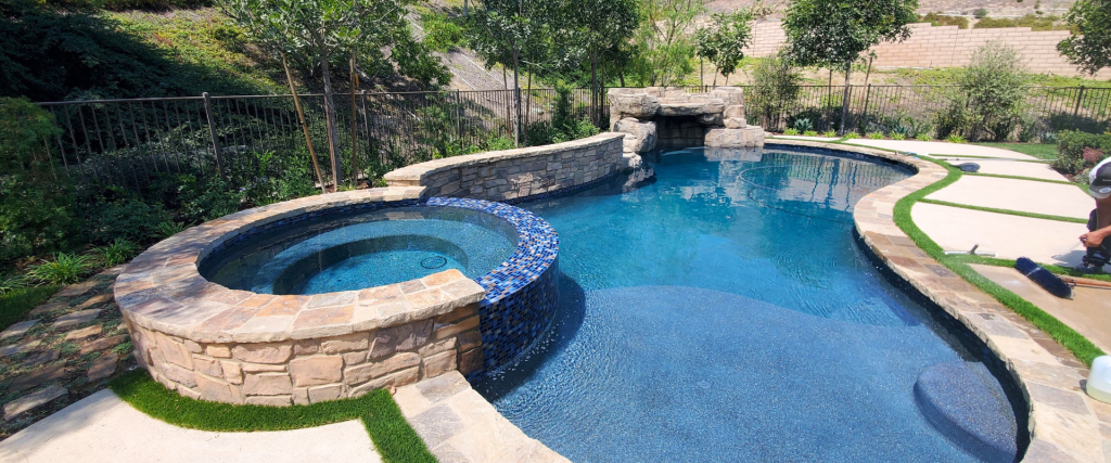 Custom freeform pool remodel with built-in spa, blue glass tile coping, and stone wall